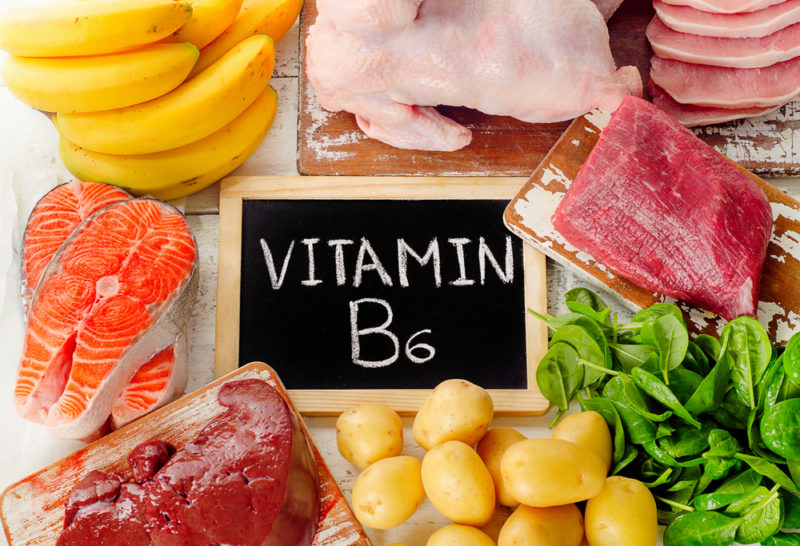 Various vitamin B6 foods surrounding a chalk board. The foods include meat and bananas