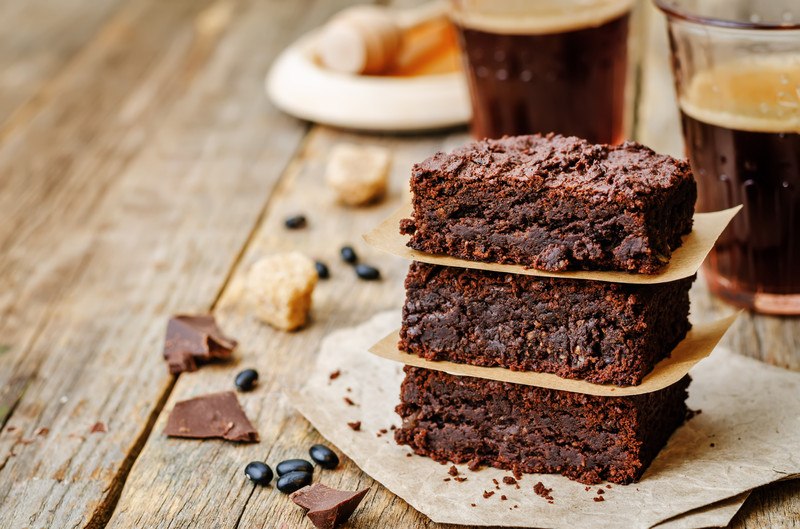 three vegan brownies stacked with cup of coffee in background