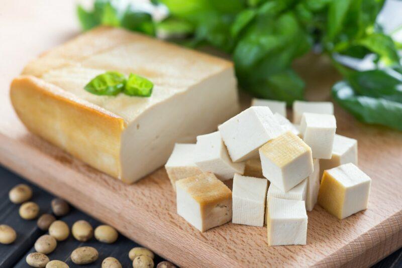 A block of vegan tofu cheese, with soy beans on the table underneath