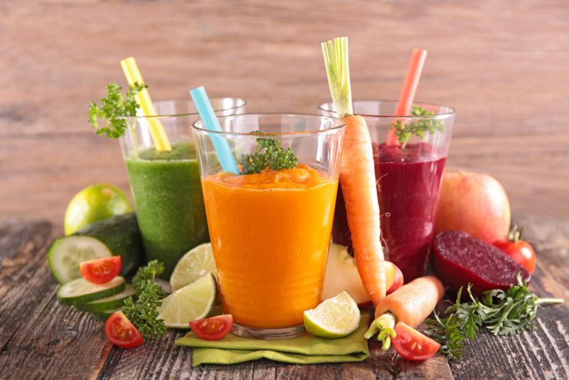 A selection of three vegetable juices and various vegetables on a table