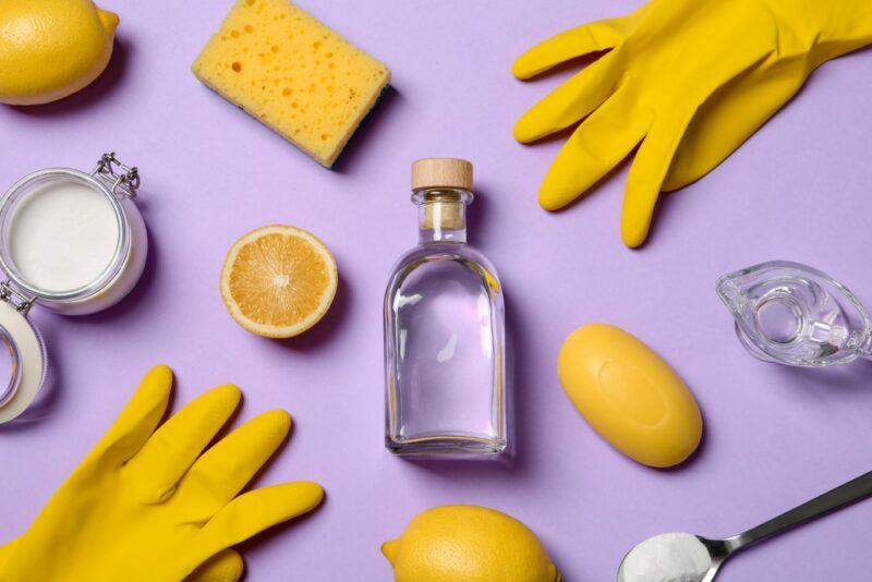 A purple table with yellow gloves and sponges, with lemons, vinegar, and baking soda for cleaning