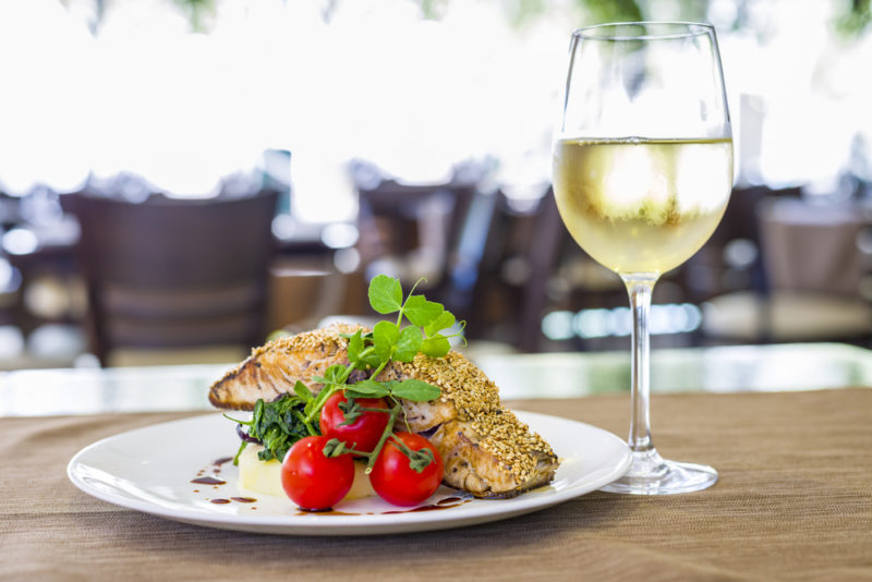 A glass of white viognier wine next to baked salmon on a plate