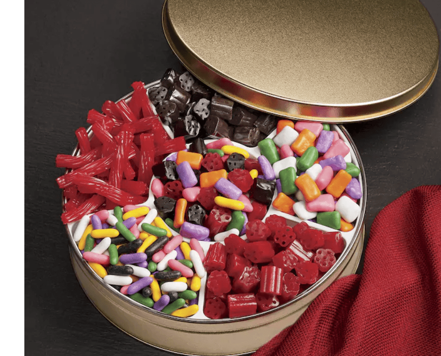 Round gold tin with plastic divider with six types of licorice, from upper left to right, red twists, black nuggets, pastel candy coated, red bites, Pastilles, and in the middle an assortment