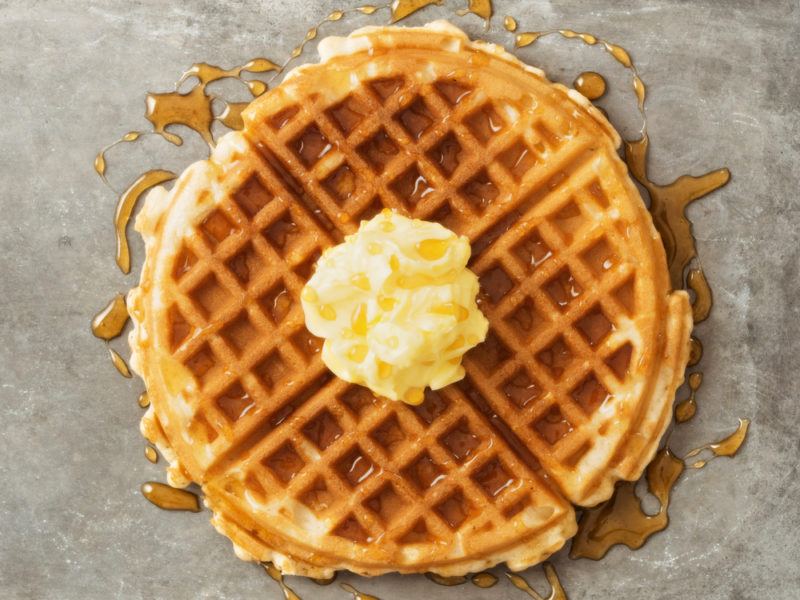 A large waffle sliced into four pieces on a table with butter