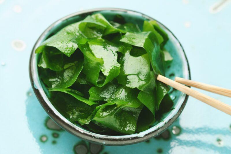 on a blue surface is a blue ceramic bowl with brown rim full of wakame