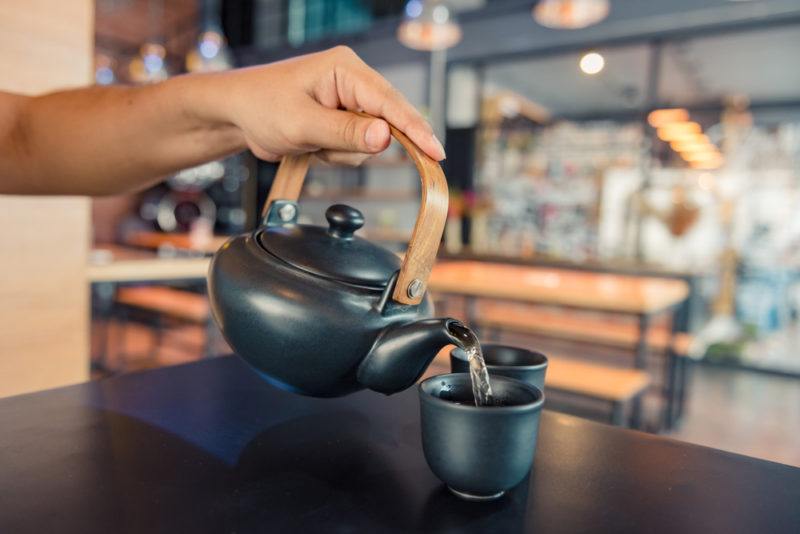 Warm water being poured into a black cup from a teapot