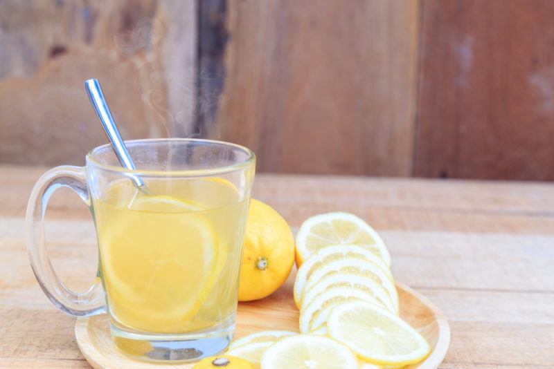 A glass of warm water with lemon and slices of lemon on the plate