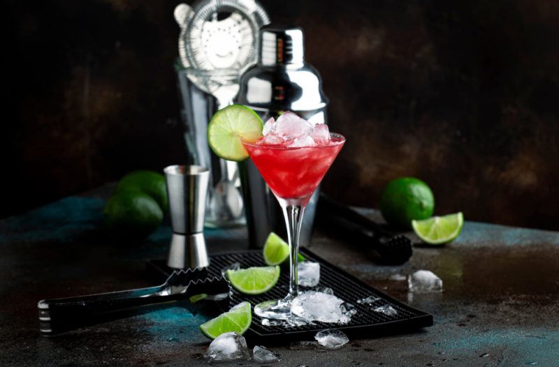 A watermelon cocktail on a counter with a shaker and a black background