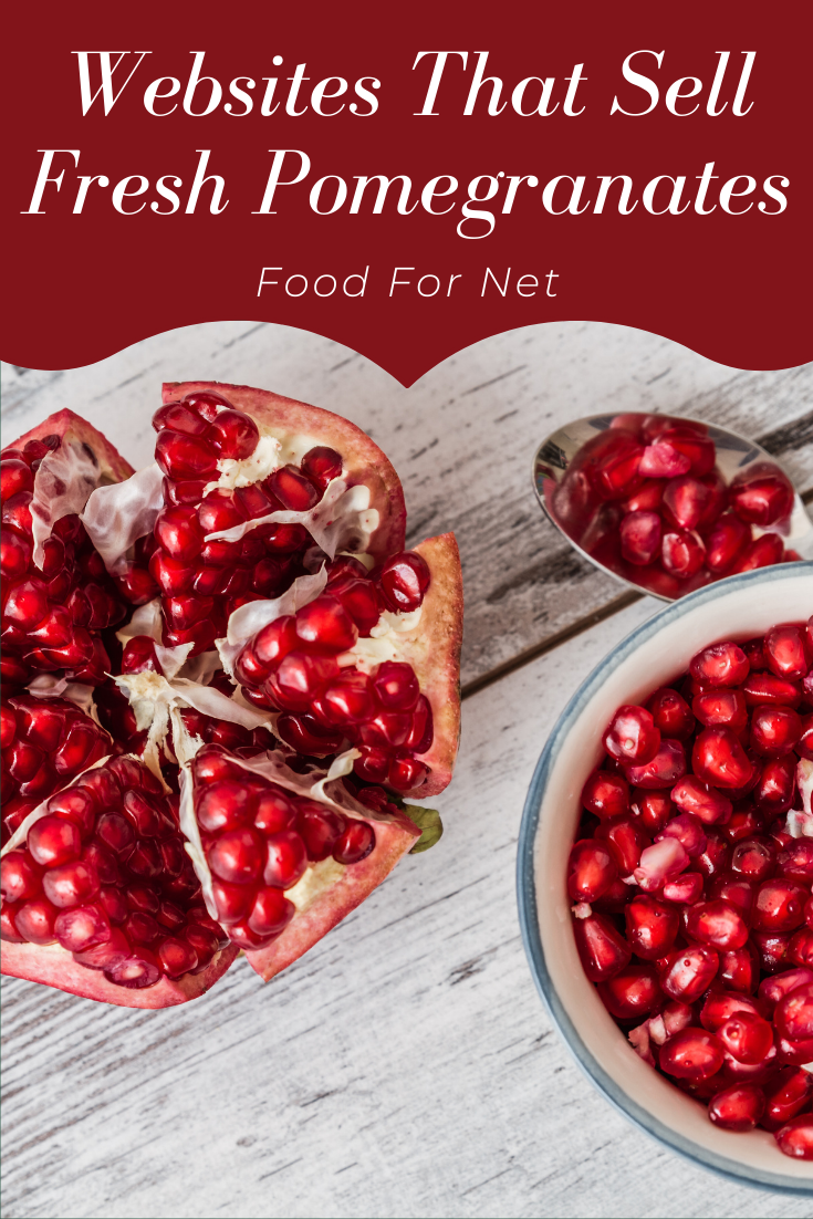 A pomegranate that has been opened and is lying on a table, next to a bowl of pomegranate arils and a spoon of the arils