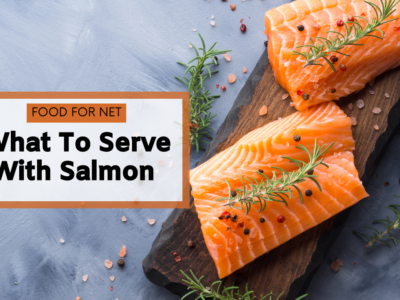 A wooden board with two raw pieces of salmon, pepper, and herbs, looking at what to serve with salmon
