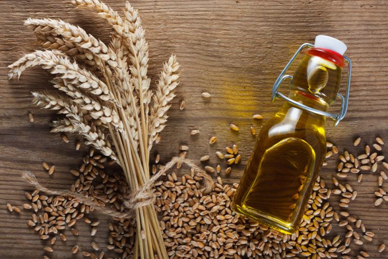 A small glass bottle of wheat bran oil, next to wheat and various grains