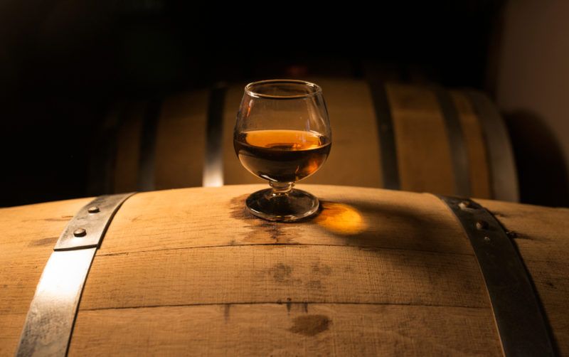 A glass of whiskey on top of an oak barrel