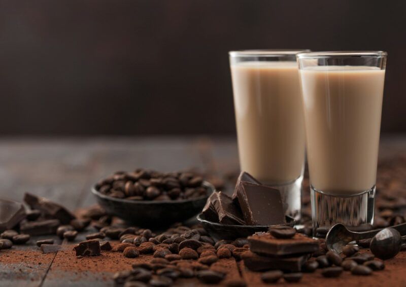 Two glasses containing whiskey peanut butter cup shots on a table with chocolate and coffee beans