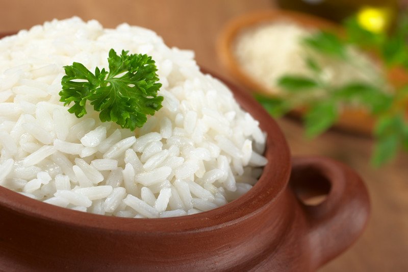 A brown bowl is filled with cooked white rice with a sprig of parsley as a garnish.