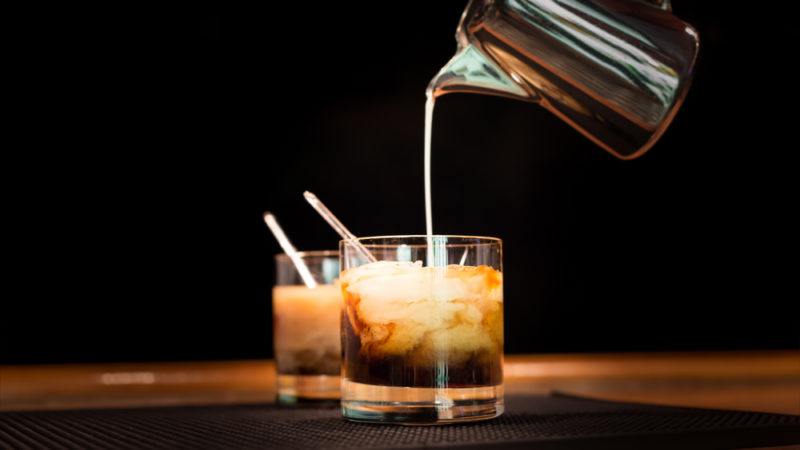 Two white Russian cocktails with milk being poured in