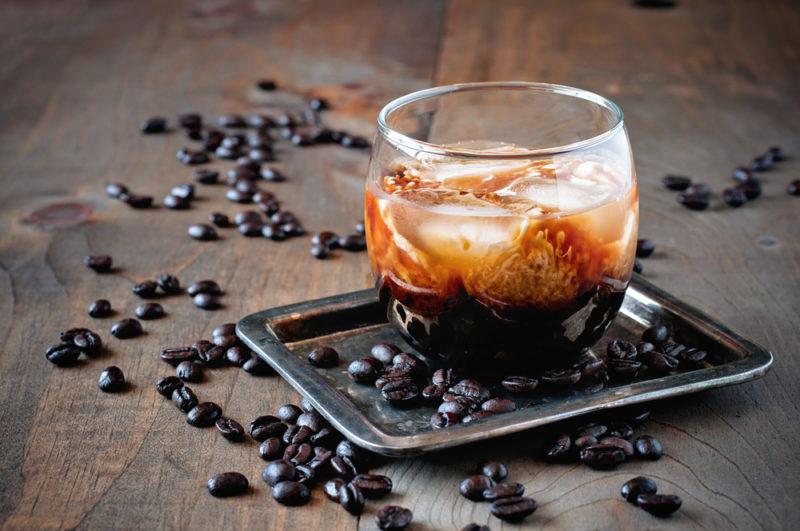 A white Russian cocktail on a slate with coffee beans around it