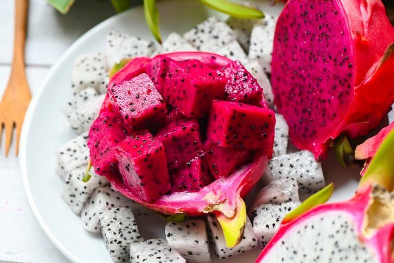 A white plate with link and white chunks of dragon fruit, along with some dragon fruit halves