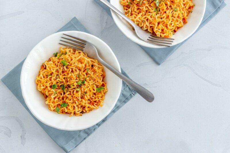 Two white plates with ramen noodles and veggies, with a fork on one of them