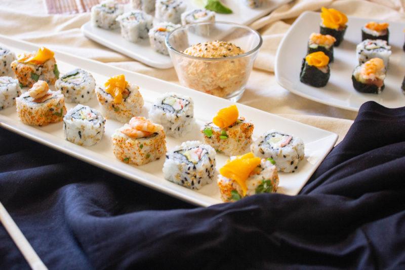 White plates with fresh sushi near some dip and a blue cloth