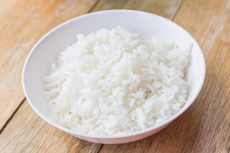 on a wooden surface is a white bowl with cooked white rice