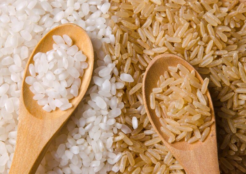 White and brown rice on a table with spoons in each that contain more rice