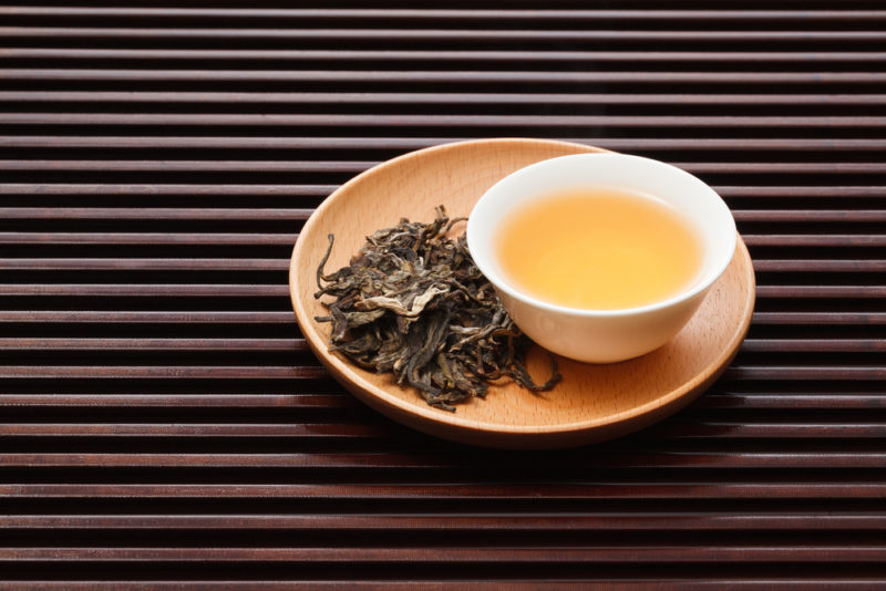 A light brown plate with white tea leaves and white tea in a mug