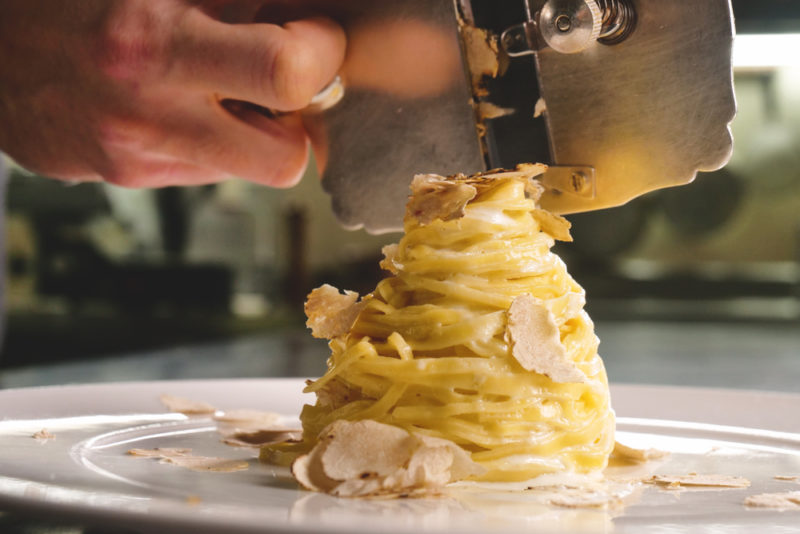 A chef thinly slicing white truffles onto an egg pasta dish