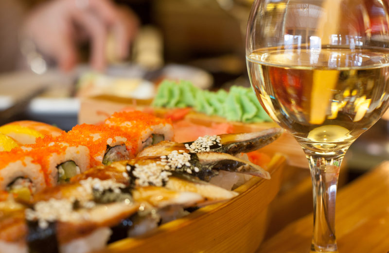 A wooden board with sushi next to a glass of wine