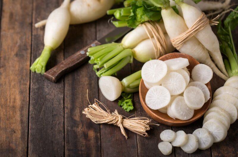 A wooden table with a collection of white radishes. Some of them are whole, while others have been sliced into small pieces