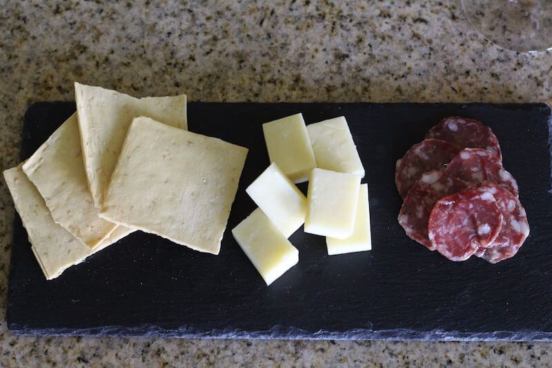 wheat crackers, white cheese, and salami on a stone plate for serving