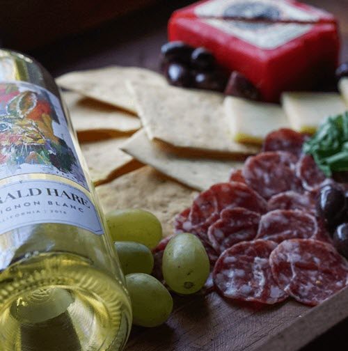 A cutting board with meat, cheese, fruit and crackers