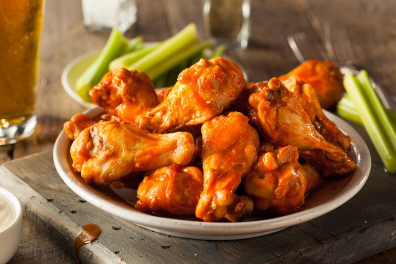 A dish of chicken wings rests on a wooden surface near some celery sticks.