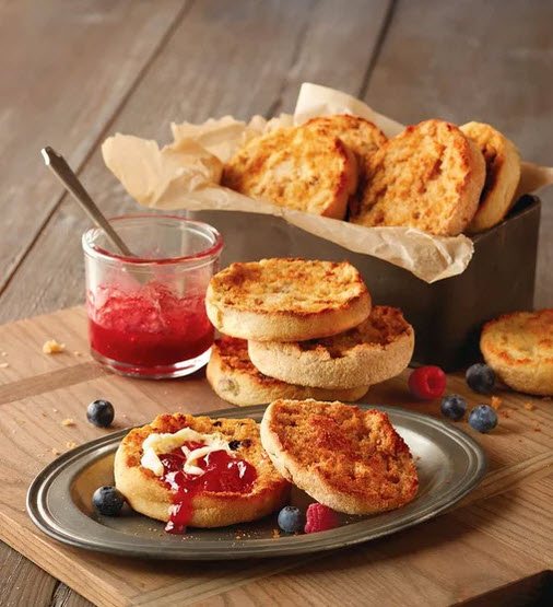 A selection of English muffins on a plate and in a wooden container, one with jam spread on it