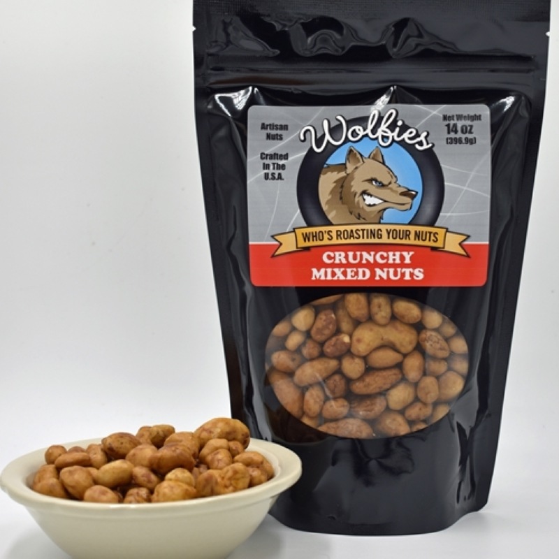 A black bag with the Wolfies logo and label for crunchy mixed nuts to the left of the bag is a white ceramic bowl full of mixed crunchy nuts