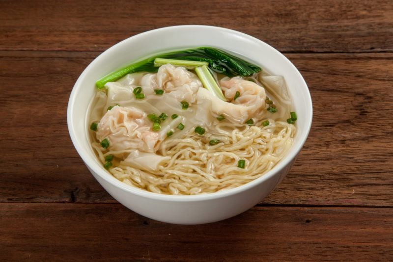 A white bowl that contains wontons, noodles, and soup