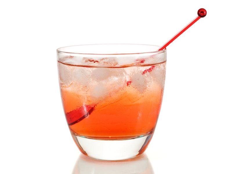 A glass of a Woo Woo cocktail with a red spoon isolated on white