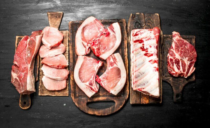 A black table with wooden boards that contain various cuts of raw pork