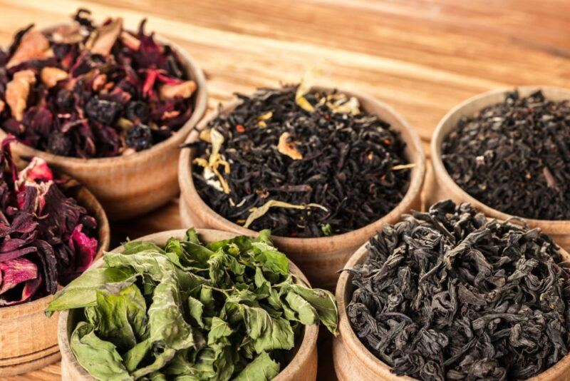 Six wooden bowls containing various types of tea leaves and herbal teas