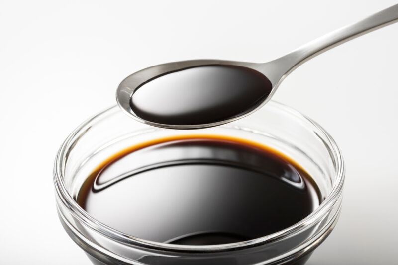 a closeup image of a small clear glass bowl of Worcestershire sauce with a silver spoon over it with Worcestershire sauce