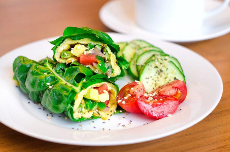 A white plate with a wrap that uses spinach on the outside