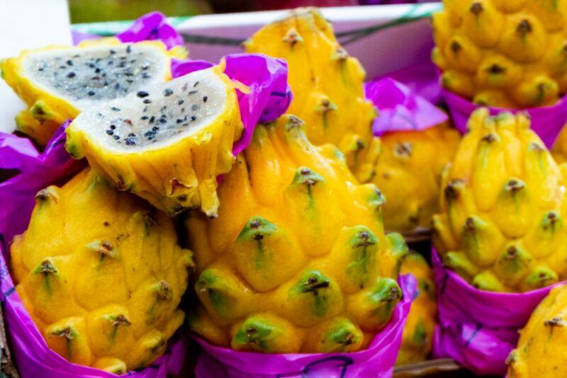 A selection of bright yellow dragonfruit in purple paper, one of which has been cut open