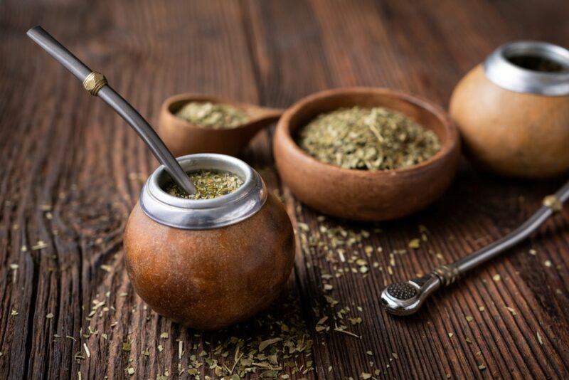 A gourd containing yerba mate, with a bowl of the leaves and a wooden spoon