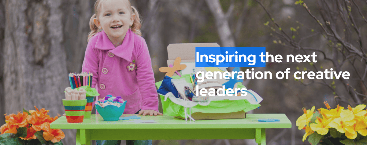 Little girl standing outside at a green kids size picnic table, crafts are on the table including a green kid crafts box on the table with flowers on both sides of the table - on the right side of the photo it said Inspiring the next generation of creative leaders