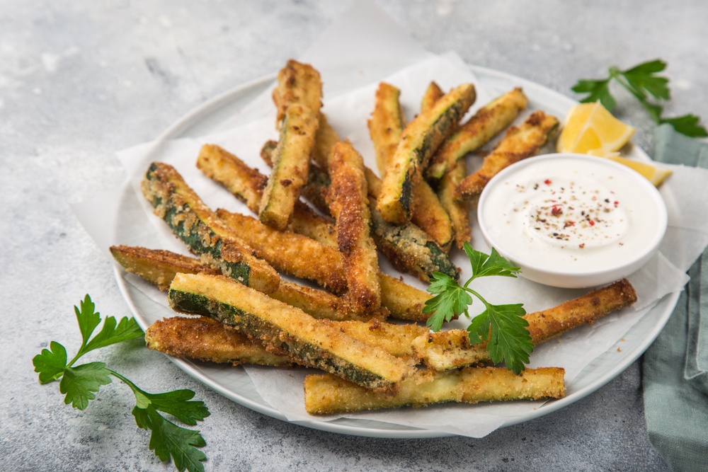 A white plate filled with zucchini fries and a bowl of white dip