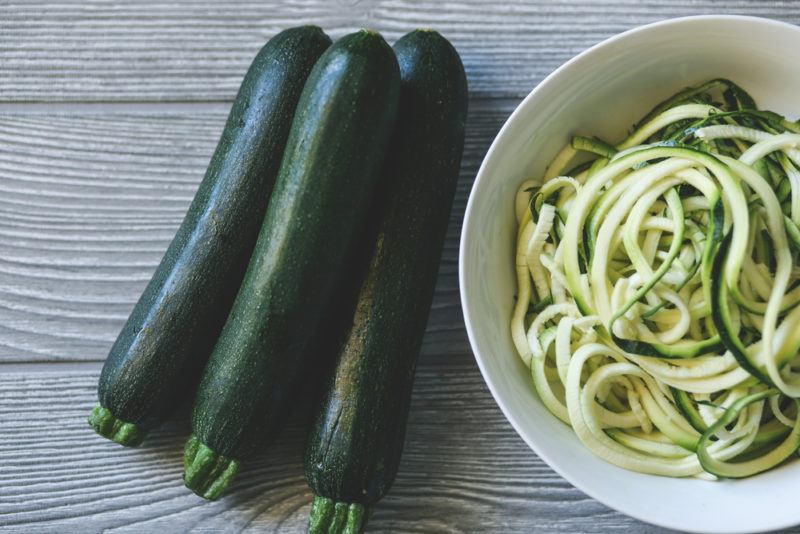 A bowl of zoodles next to three zucchinis