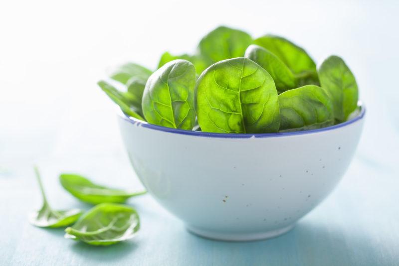 a white bowl full of baby spinach leaves