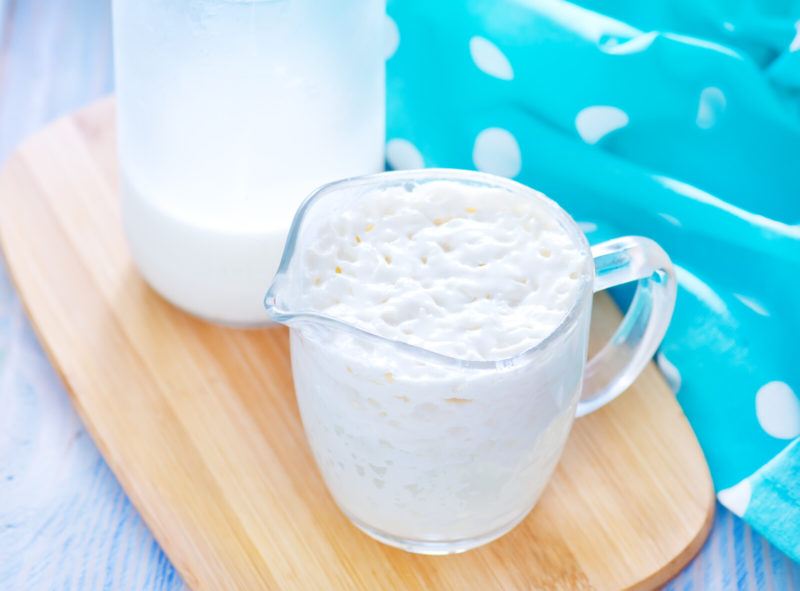 a clear jug and a clear glass with kefir on top of a chopping board with a white and blue polka-dotted table napkin