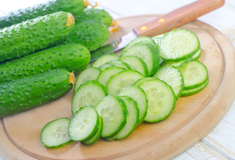 Whole Japanese cucumbers plus sliced cucumbers on a wooden chopping board