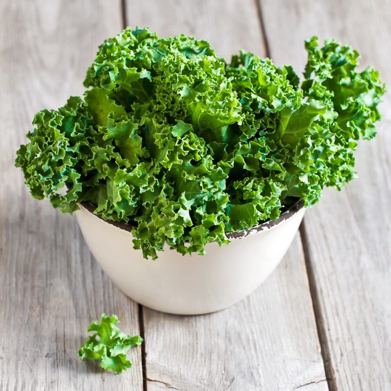 a deep white bowl filled with kale, placed on a wodden table