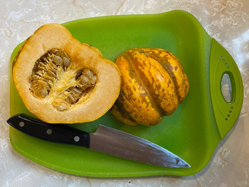 overhead shot of a green plastic chopping board with a halve acorn squash and a knife beside it